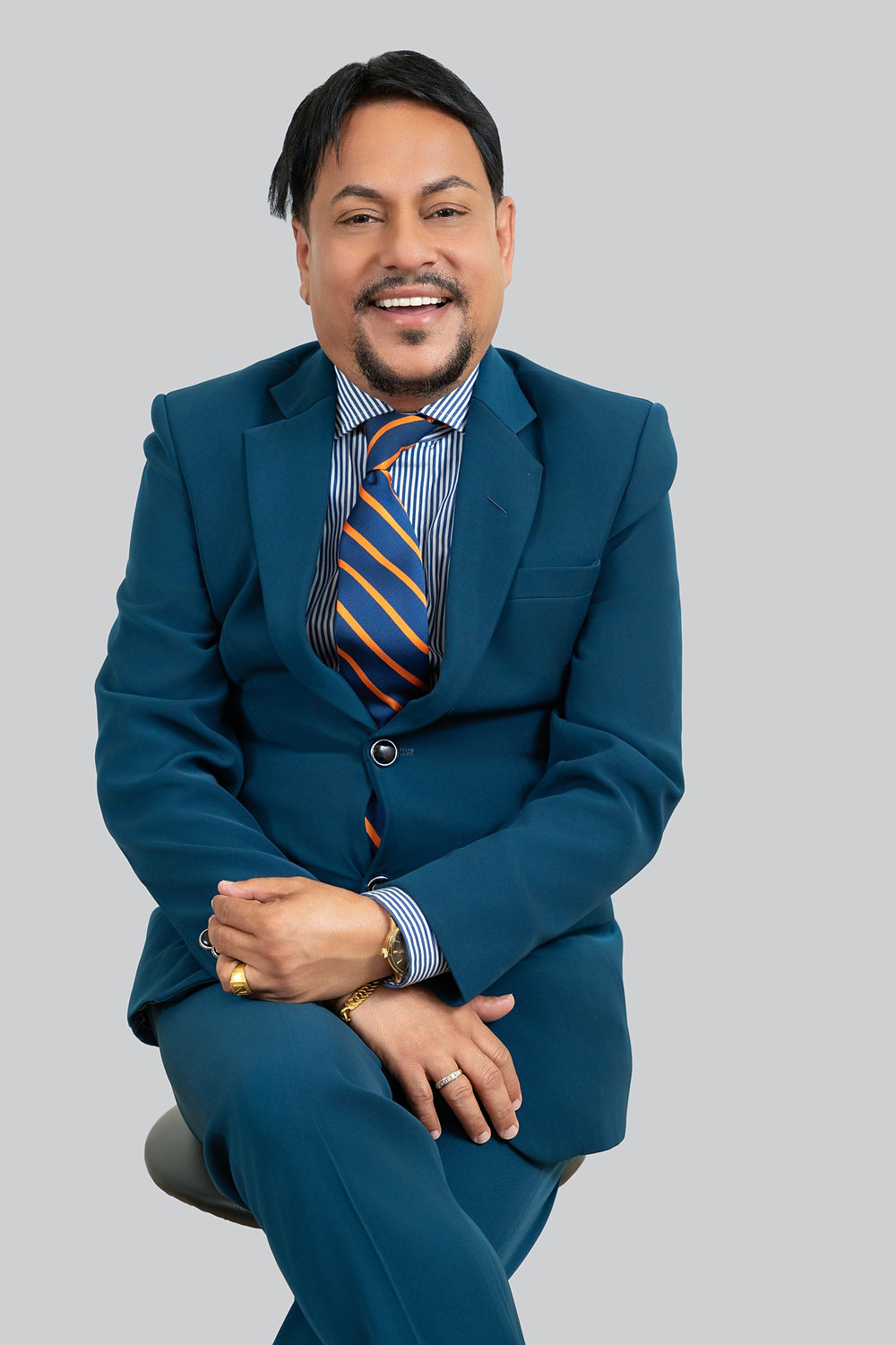 Studio headshot of a smiling professional in a blue suit and striped tie against a gray backdrop