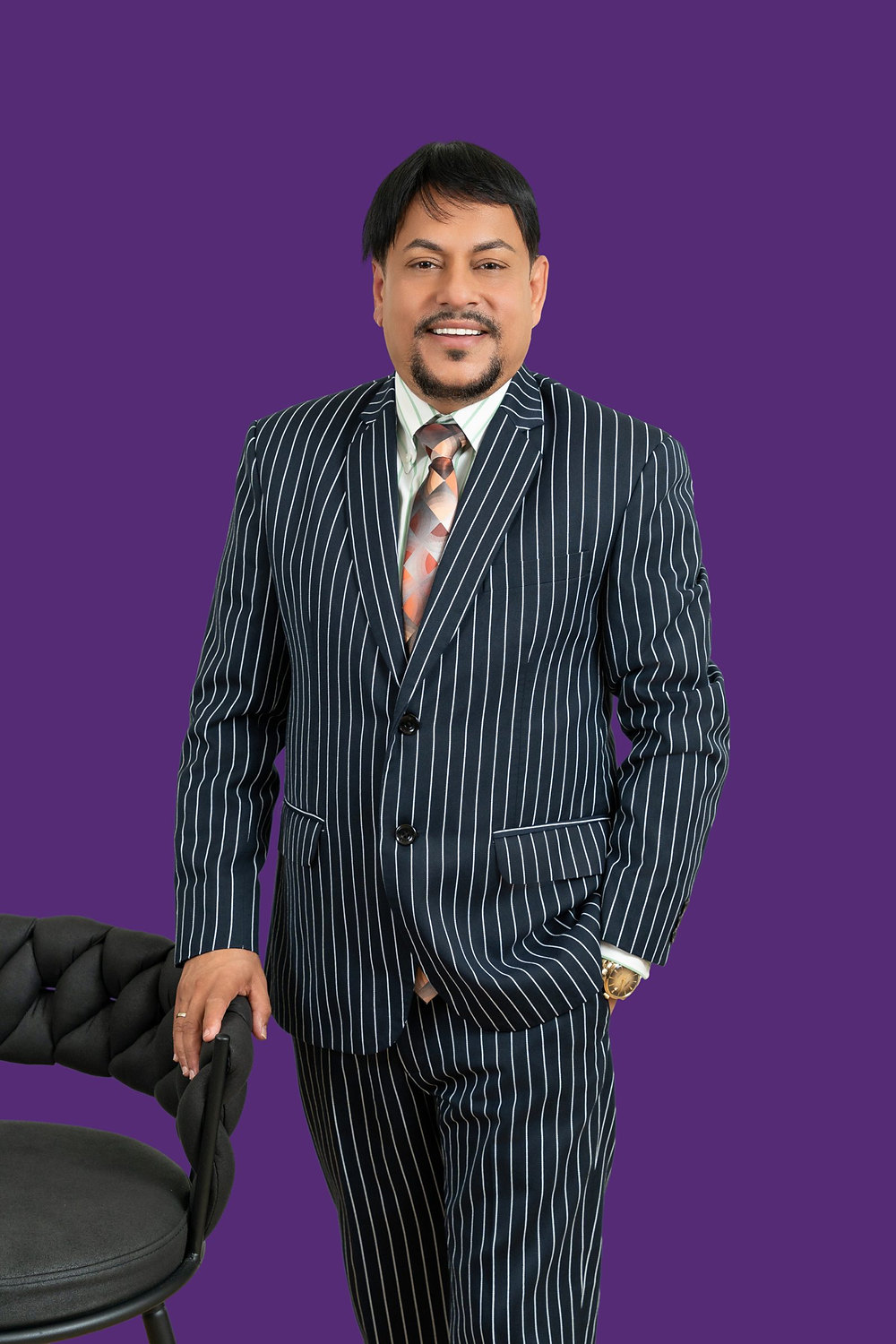 Studio headshot of a businessman in a pinstripe suit against a purple backdrop