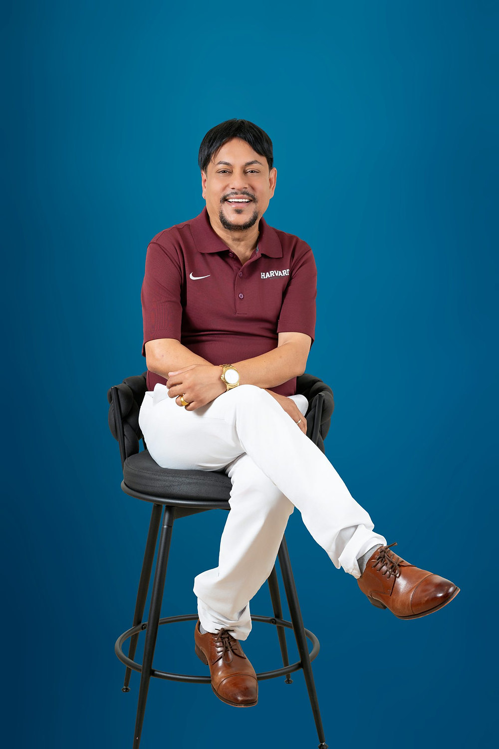 Full-length studio portrait of a businessman seated on a stool against a blue backdrop